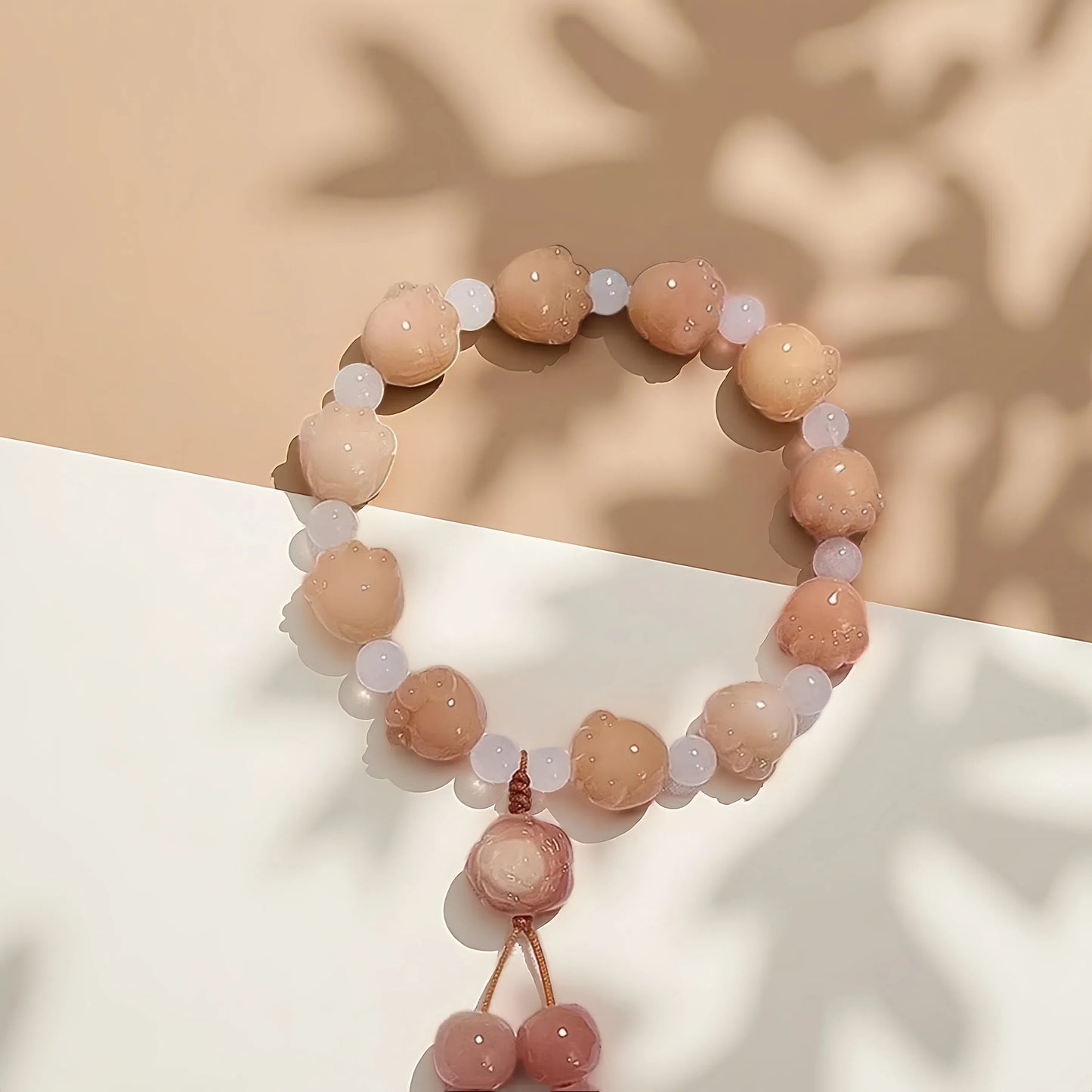 The 24 Solar Terms Series TAOÉ Pawfect Bodhi Bracelet: Carved Cat Paw Pendant - Autumnal Equinox features alternating peach and white beads with a cat-paw accent, arranged in a circle on a beige and white background with leaf shadows.
