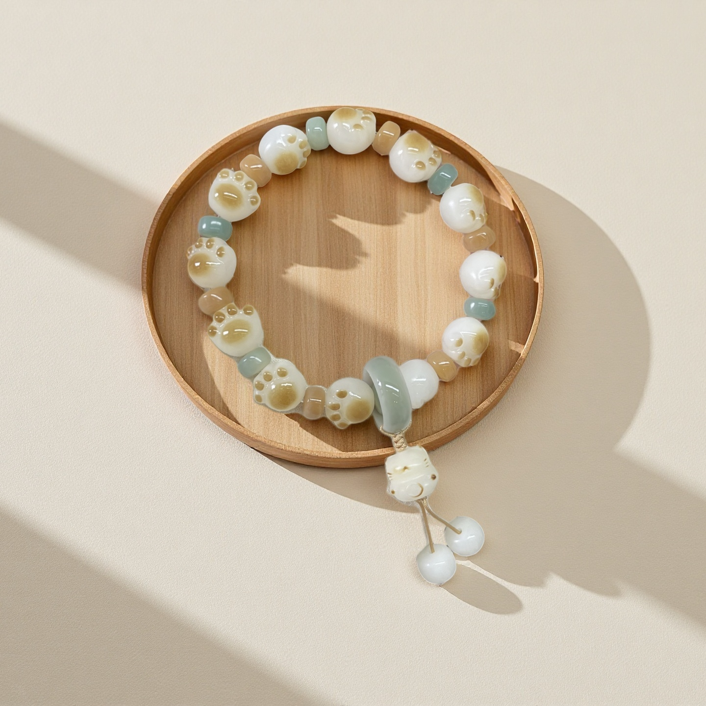 The 24 Solar Terms Series TAOÉ Pawfect Bodhi - Winter Solstice Whisker Bracelet features white and light blue beads shaped like cat paws and faces, with a subtle whisker motif, shown on a wooden tray against a beige background.