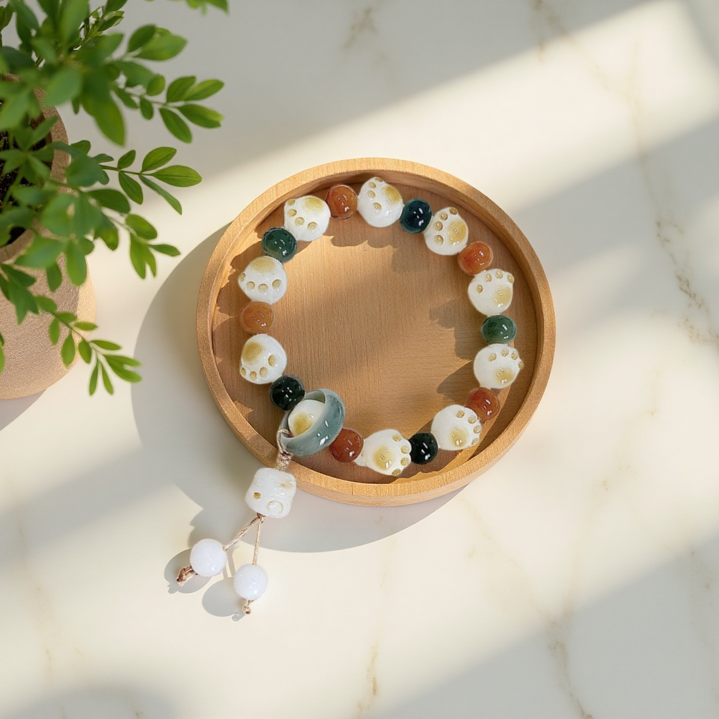 The 24 Solar Terms Series TAOÉ Pawfect Bodhi - Start of Summer Lime Green Bracelet, featuring white cat paw beads and orange-brown bodhi wood, is displayed on a round wooden tray near a potted plant under sunlight.