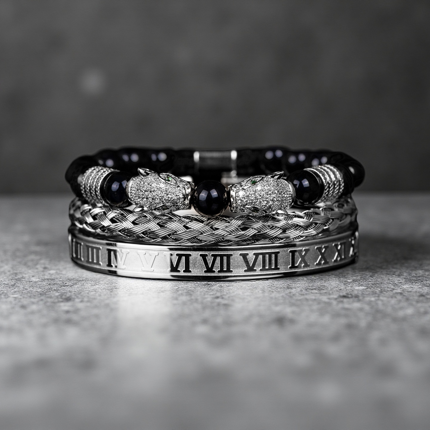 A stack of three luxury bracelets from the Five Elements Series: the TAOÉ Gothic Black Panther Braid, a Silver Steel Numeral Cuff, and a metallic beaded bracelet with gem accents on a stone surface.