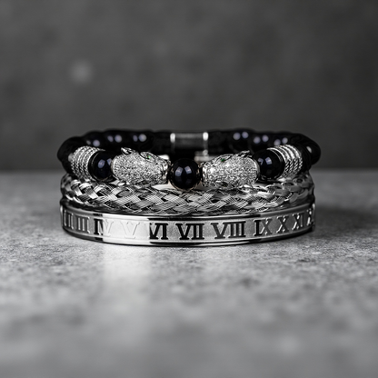 A stack of three luxury bracelets from the Five Elements Series: the TAOÉ Gothic Black Panther Braid, a Silver Steel Numeral Cuff, and a metallic beaded bracelet with gem accents on a stone surface.