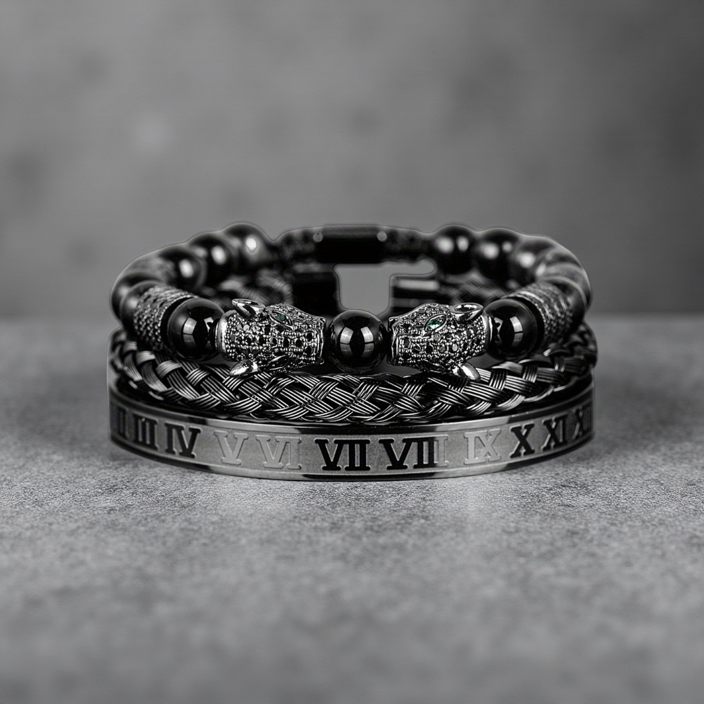 The Five Elements Series TAOÉ Gothic Black Panther Braid + Silver Steel Numeral Bracelet Set-Metal features a braided black panther bracelet, a sleek silver Roman numeral cuff, and other bold designs on a gray surface.