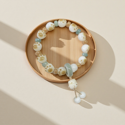 The 24 Solar Terms Series TAOÉ Pawfect Bodhi - Winter Solstice Whisker Bracelet features white and light blue beads shaped like cat paws and faces, with a subtle whisker motif, shown on a wooden tray against a beige background.